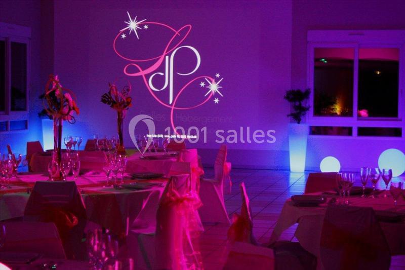 Salle de réception décorée avec des tables dressées, éclairage coloré et logo projeté sur un mur.