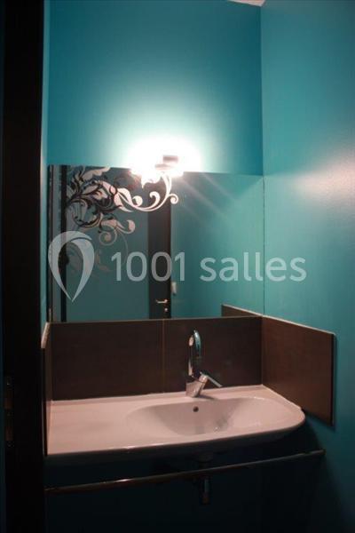 Lavabo blanc avec robinet chromé, miroir mural et éclairage au-dessus, dans une salle de bain aux murs bleu turquoise.