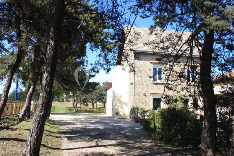 Maison en pierre avec toit en tuiles, entourée d'arbres, au bout d'une allée gravillonnée sous un ciel bleu.
