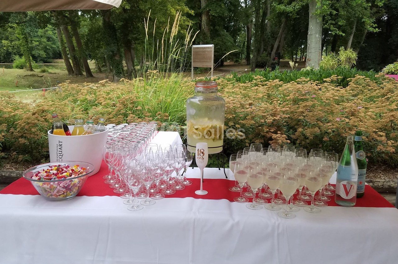 Table dressée en extérieur avec des verres, une jarre de citronnade, des bonbons et des bouteilles d'eau.
