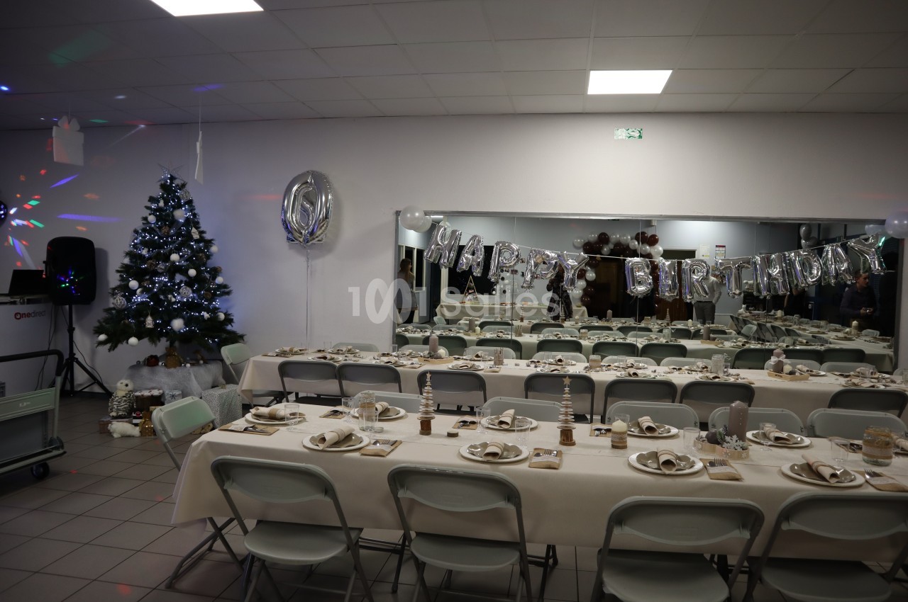 Salle décorée pour un anniversaire avec tables dressées, guirlande ’Happy Birthday’ et sapin illuminé.