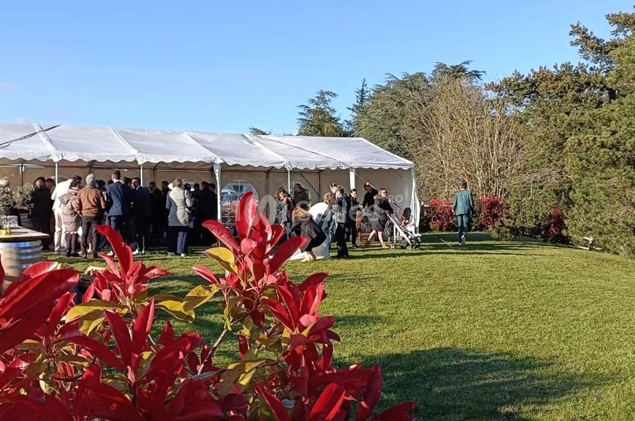 Groupe de personnes rassemblées près d'une tente blanche dans un jardin verdoyant par une journée ensoleillée.