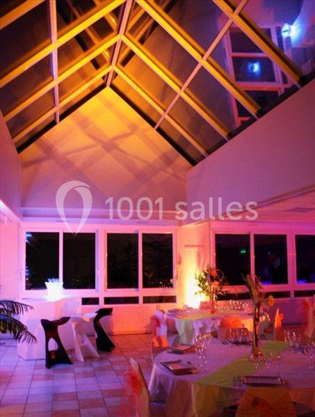 Salle lumineuse avec verrière, éclairage coloré et tables décorées pour un événement festif.