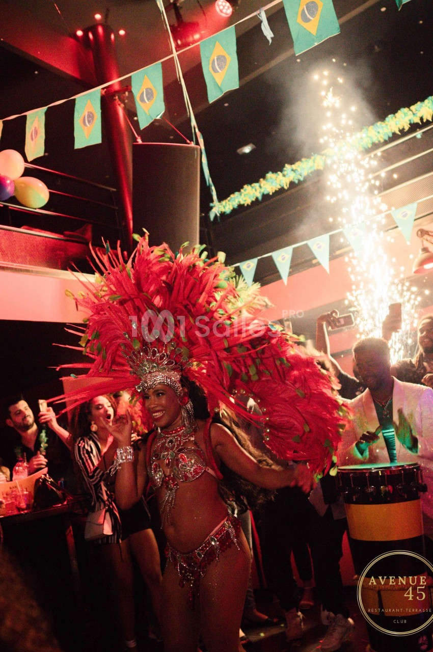 Danseuse en costume de carnaval rouge avec plumes, performe dans une ambiance festive sous des drapeaux brésiliens.