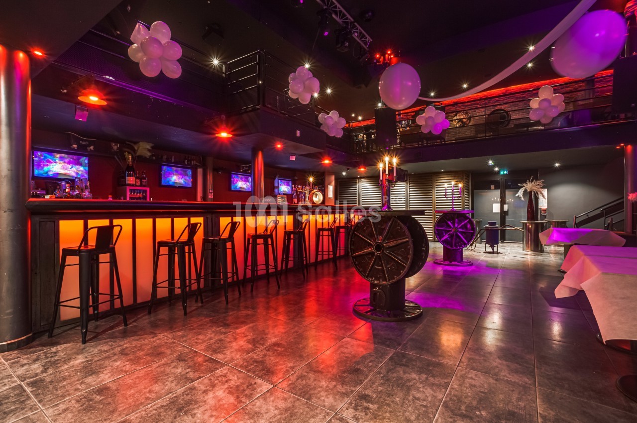 Salle de bar décorée avec des lumières rouges, des ballons blancs et un comptoir avec des tabourets hauts.