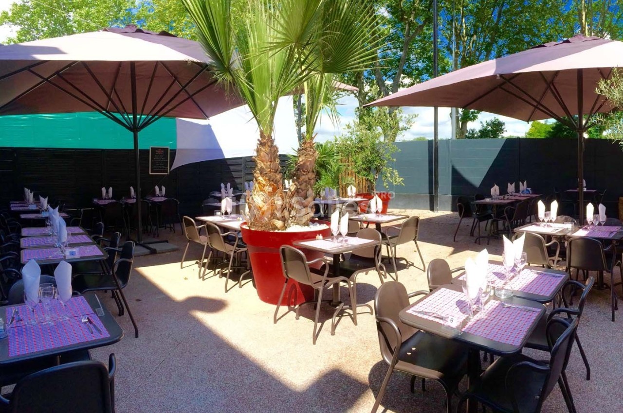 Terrasse de restaurant avec tables dressées, parasols et végétation, sous un ciel dégagé.