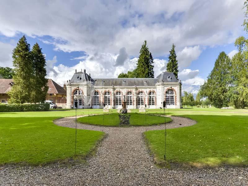 Bâtiment historique avec grandes fenêtres, entouré de pelouses, arbres et allées gravillonnées sous un ciel partiellement…