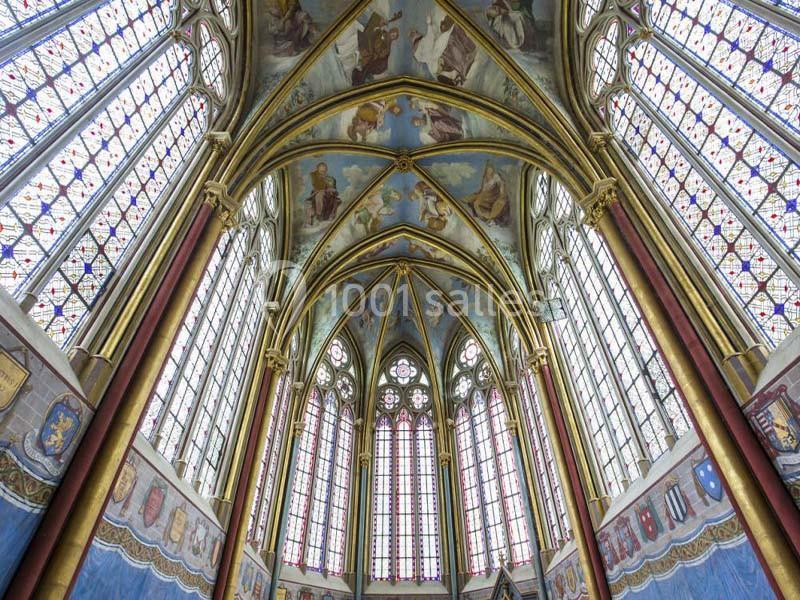 Intérieur d'une chapelle gothique avec des vitraux colorés, des voûtes ornées et des peintures murales détaillées.