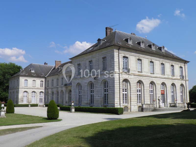 Bâtiment historique en pierre avec grandes fenêtres, entouré d'une pelouse et d'un ciel dégagé.