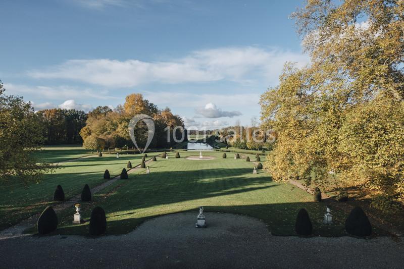Vue d'un jardin à la française avec pelouses, allées symétriques, statues et un bassin au loin, sous un ciel dégagé.
