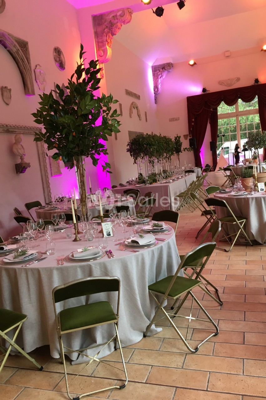 Salle de réception décorée avec des tables rondes dressées, chaises vertes et éclairage d'ambiance rose.
