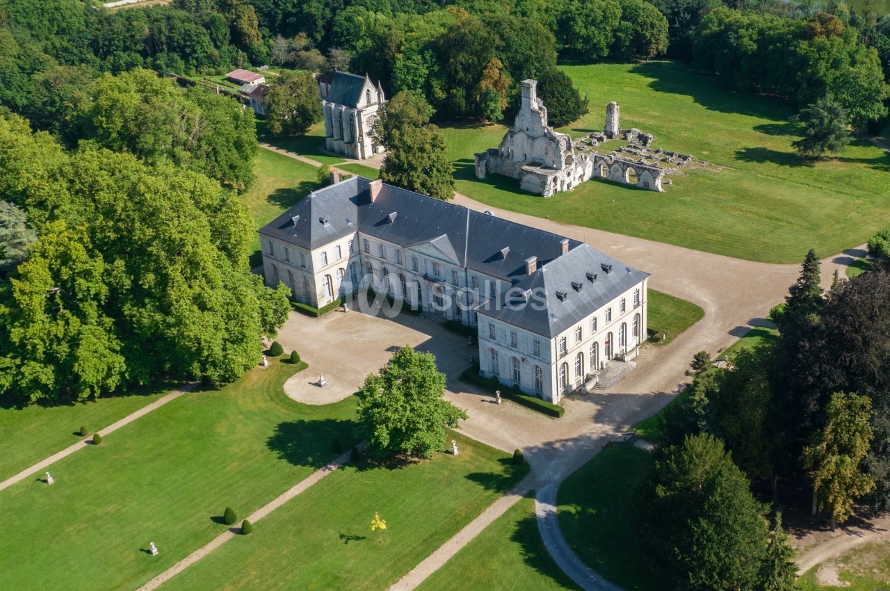 Vue aérienne d'un château entouré de jardins verdoyants et de ruines historiques dans un cadre arboré.