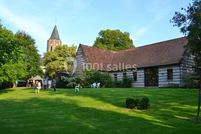 Bâtiment en briques et colombages entouré d'un jardin verdoyant, avec une église en arrière-plan.