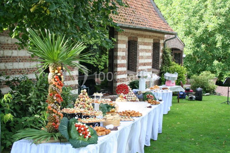 Buffet en extérieur avec tables garnies de fruits, viennoiseries et desserts, près d'une maison en briques et d'un jardin…