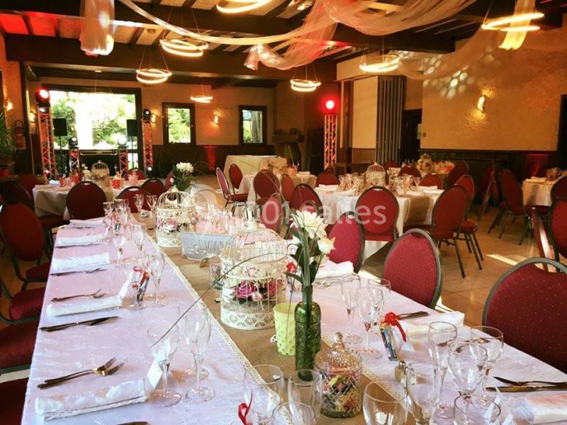 Salle de réception décorée avec des tables dressées, nappes blanches, chaises rouges et ornements floraux.