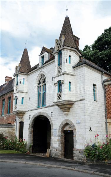 Façade d'un bâtiment historique en pierre blanche avec deux tours, une arche centrale et des fenêtres à meneaux.