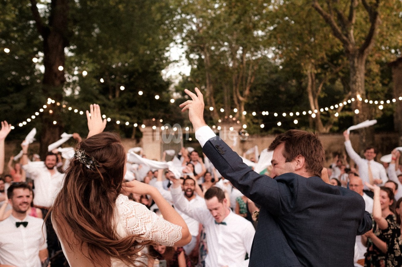 Un couple danse lors d'une fête en plein air, entouré d'invités joyeux sous des guirlandes lumineuses.