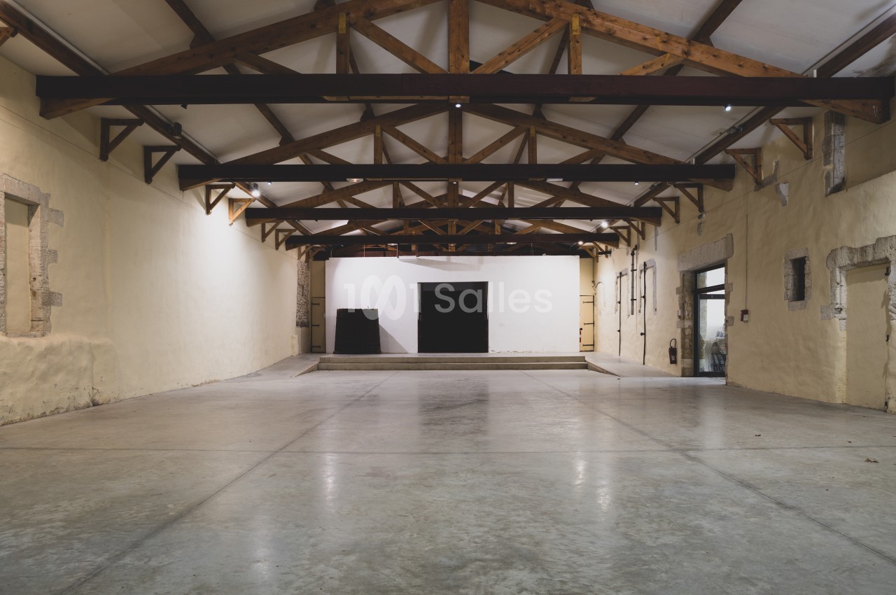 Intérieur d'un grand espace vide avec plafond en poutres apparentes et murs en pierre claire.