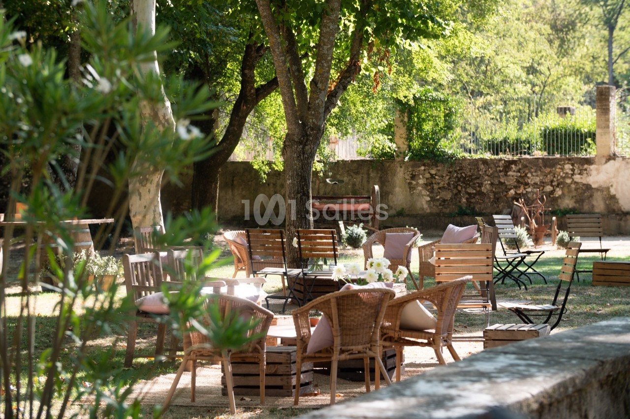 Mobilier de jardin en bois et rotin disposé sous des arbres dans un espace extérieur ombragé.