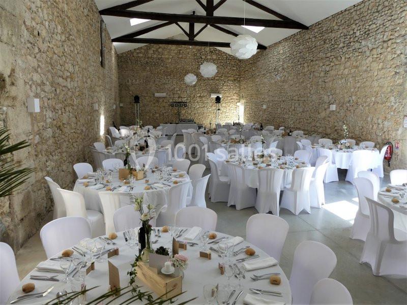 Salle de réception en pierre avec des tables rondes dressées pour un événement, décorées de nappes blanches et de centres de…