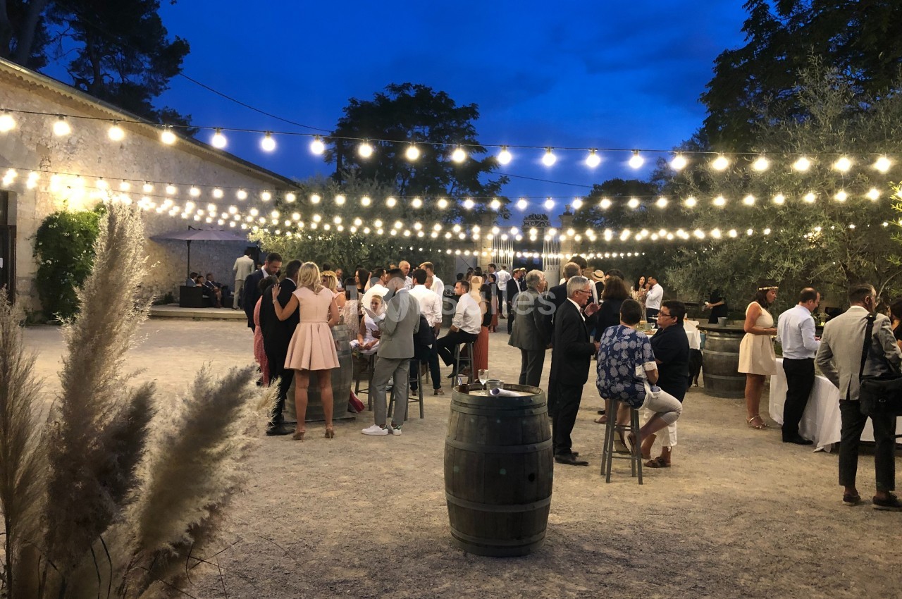 Groupe de personnes réunies en soirée dans une cour éclairée par des guirlandes lumineuses, ambiance conviviale.