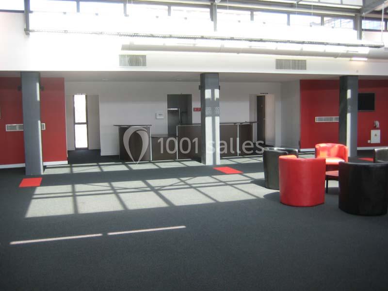 Espace intérieur lumineux avec moquette sombre, murs rouges et blancs, mobilier moderne et grandes fenêtres.