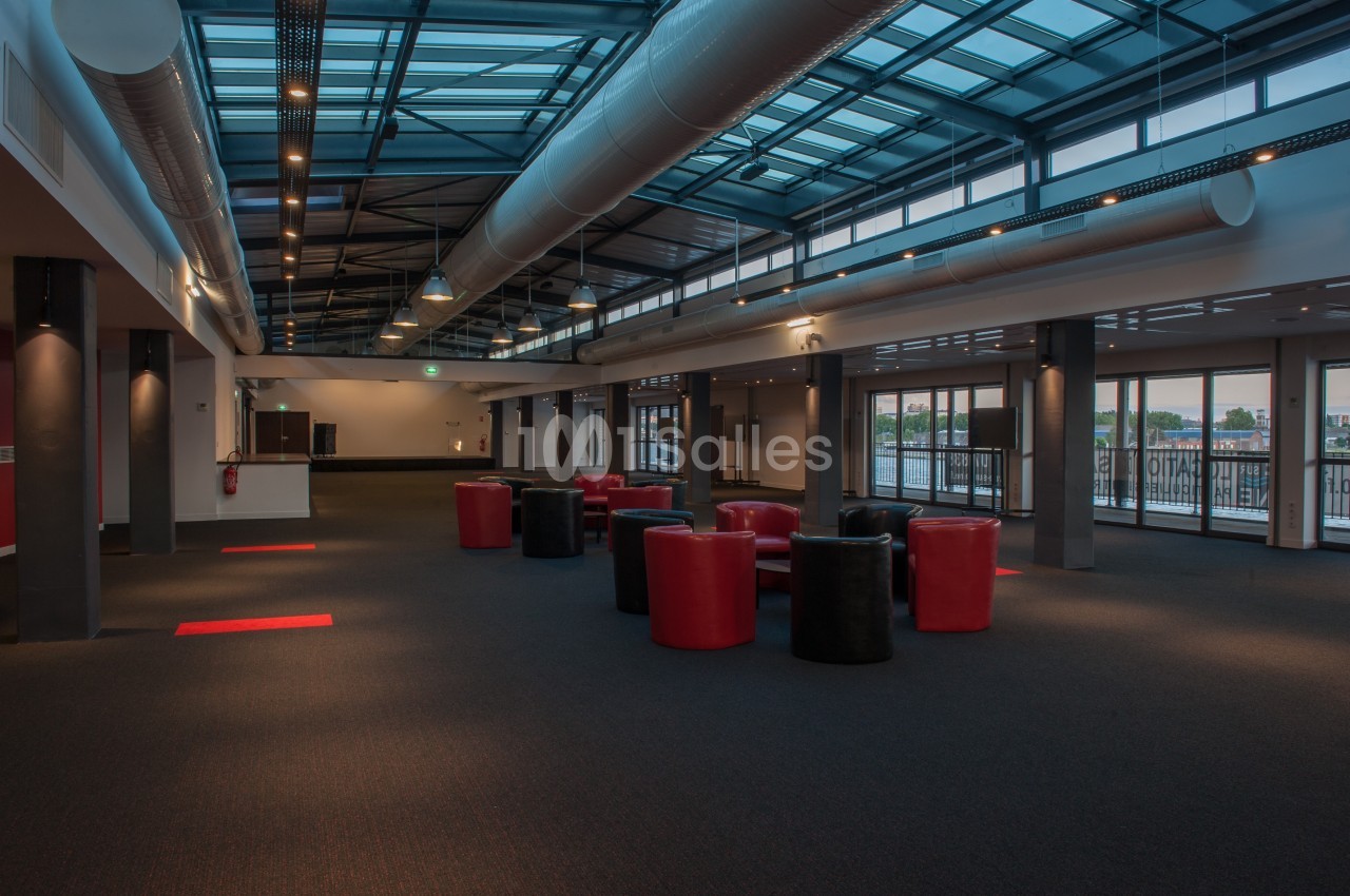 Salle spacieuse avec plafond vitré, mobilier rouge et noir, éclairage artificiel et grandes baies vitrées.