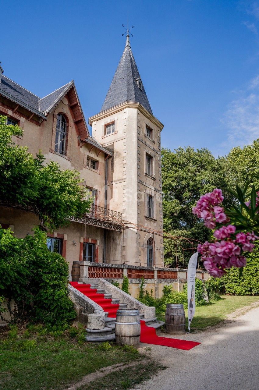 Château avec tour en pierre, tapis rouge à l'entrée, tonneaux en décoration et fleurs au premier plan.