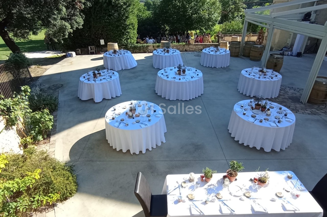 Tables rondes dressées avec nappes blanches et décorations, disposées en extérieur sur une terrasse ensoleillée.