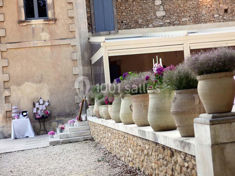 Alignement de pots en terre cuite avec des plantes fleuries devant un bâtiment en pierre, ambiance extérieure paisible.
