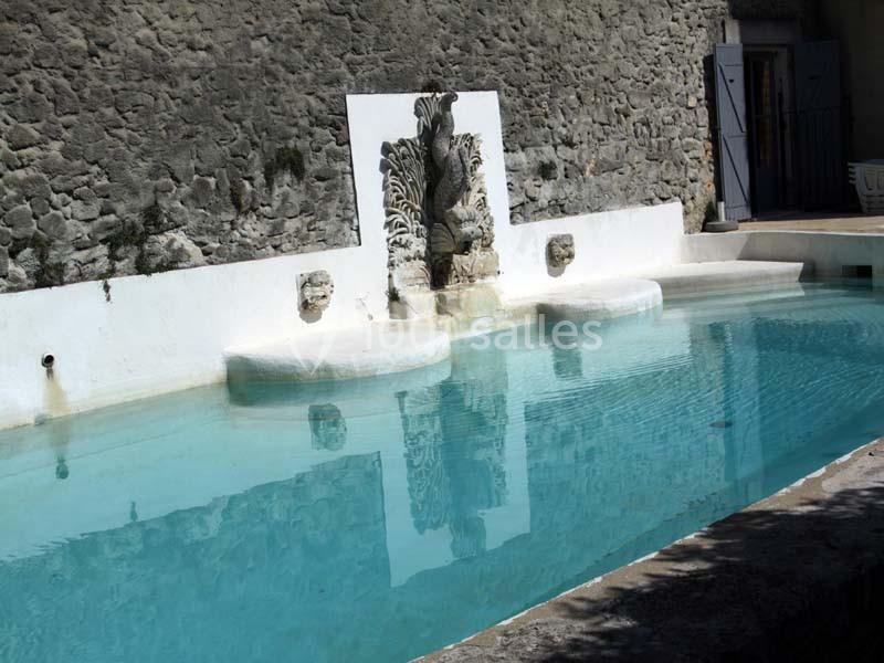 Bassin en pierre avec une fontaine ornée de sculptures, adossé à un mur en pierre, sous une lumière naturelle.