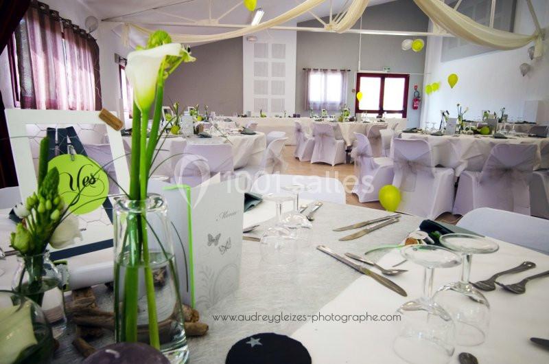 Salle de réception décorée pour un événement, avec tables dressées, fleurs blanches et ballons jaunes.