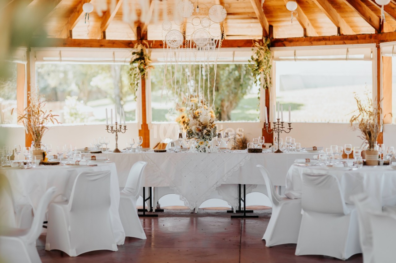 Salle décorée pour un événement avec une grande table dressée, nappes blanches, chandeliers et ornements floraux.