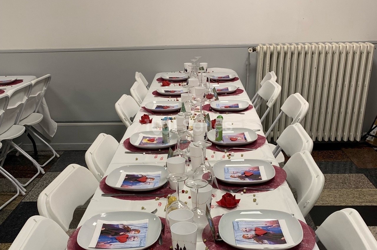 Table dressée avec des assiettes décorées, nappes blanches, pétales rouges et confettis, dans une salle sobre.