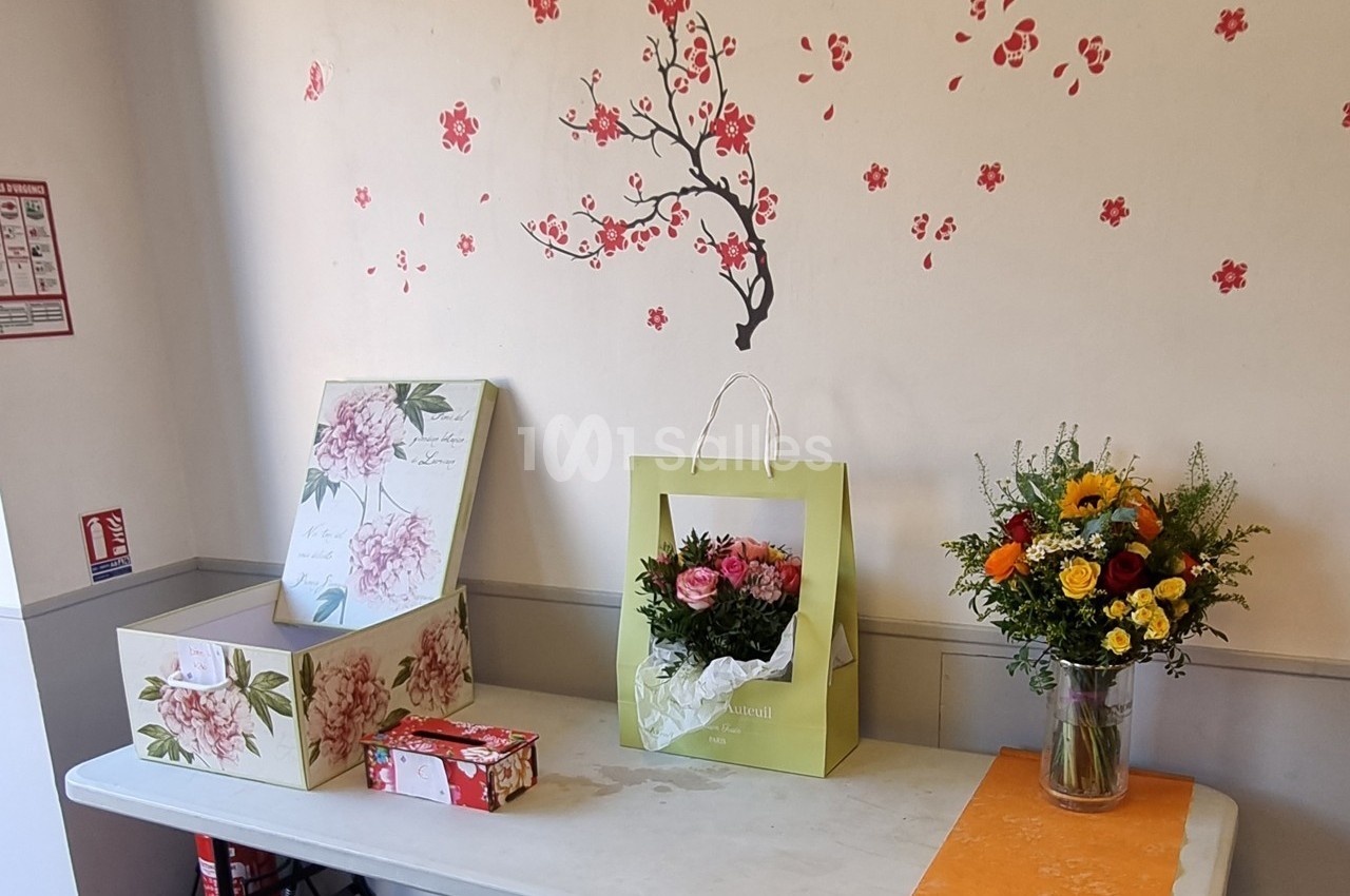 Table décorée avec des boîtes fleuries, un bouquet de fleurs dans un sac et un vase, sur fond de mur avec motifs floraux.