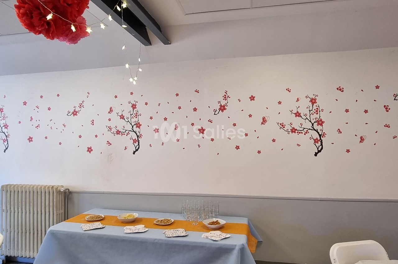 Mur décoré de motifs de branches fleuries, table dressée avec nappes colorées et petits plats dans une salle lumineuse.