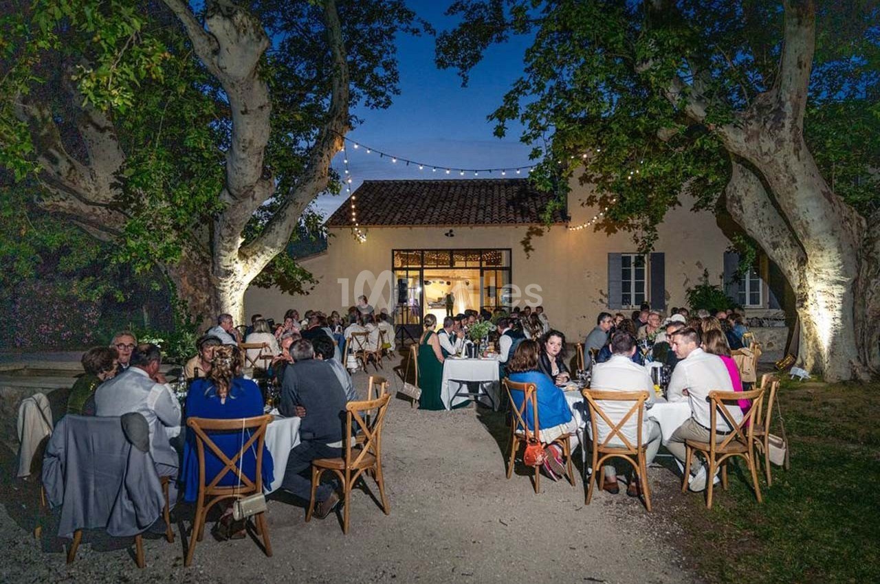Dîner en plein air sous des guirlandes lumineuses, avec des invités assis à des tables devant une maison éclairée.