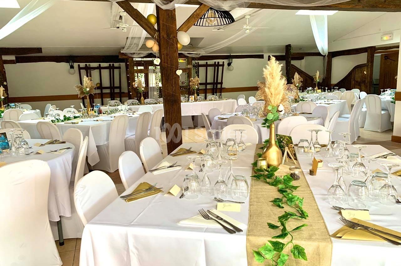 Salle de réception décorée avec des tables dressées, nappes blanches, chemins de table en lin et ornements végétaux.