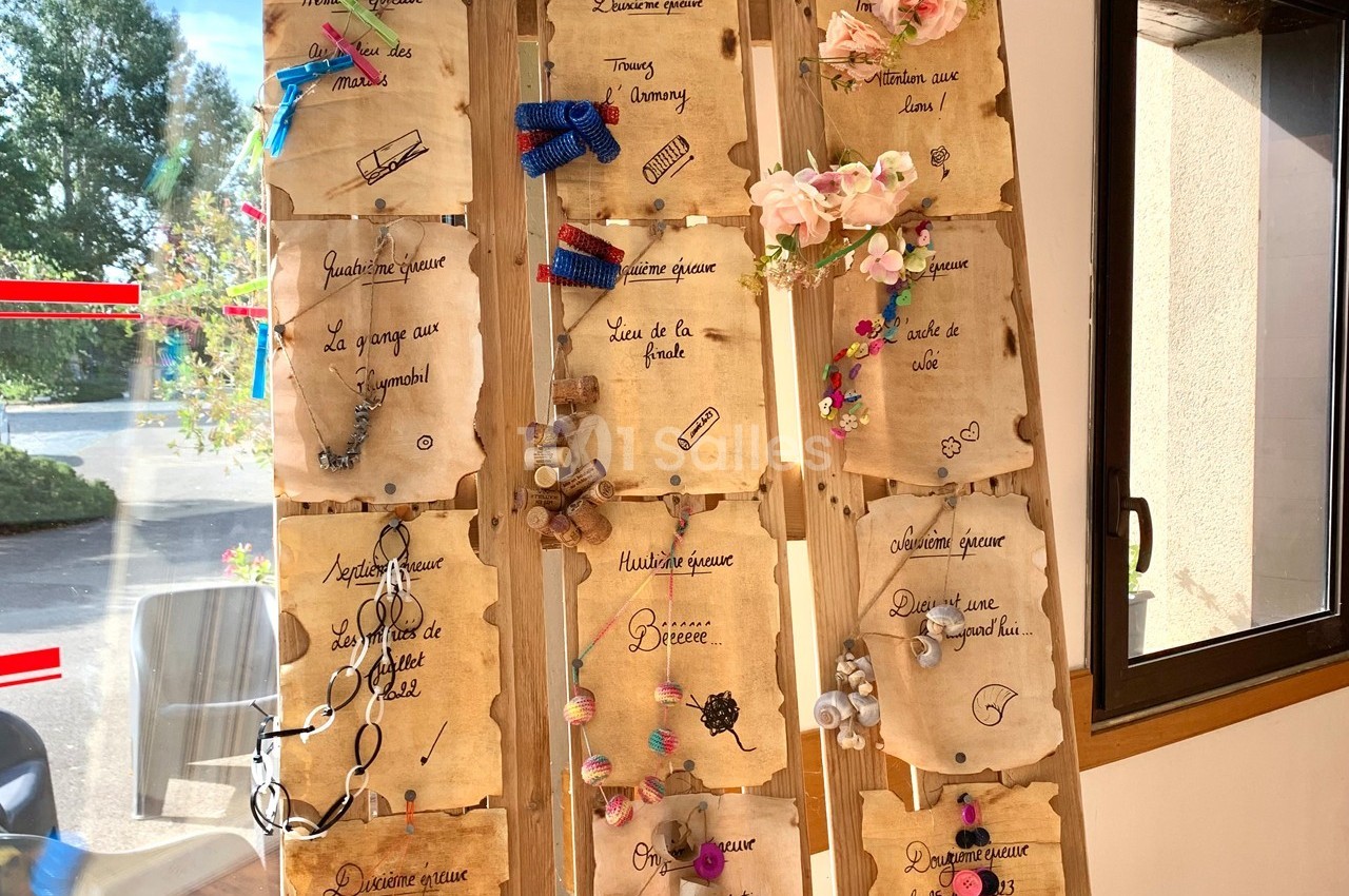 Panneau en bois décoré de parchemins manuscrits, rubans, fleurs et petits objets, exposé près d'une fenêtre.