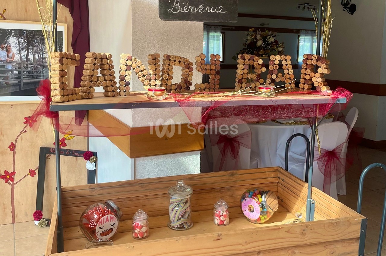 Chariot en bois décoré avec des bocaux de bonbons, une inscription ’Candy Bar’ en bouchons et des éléments festifs.