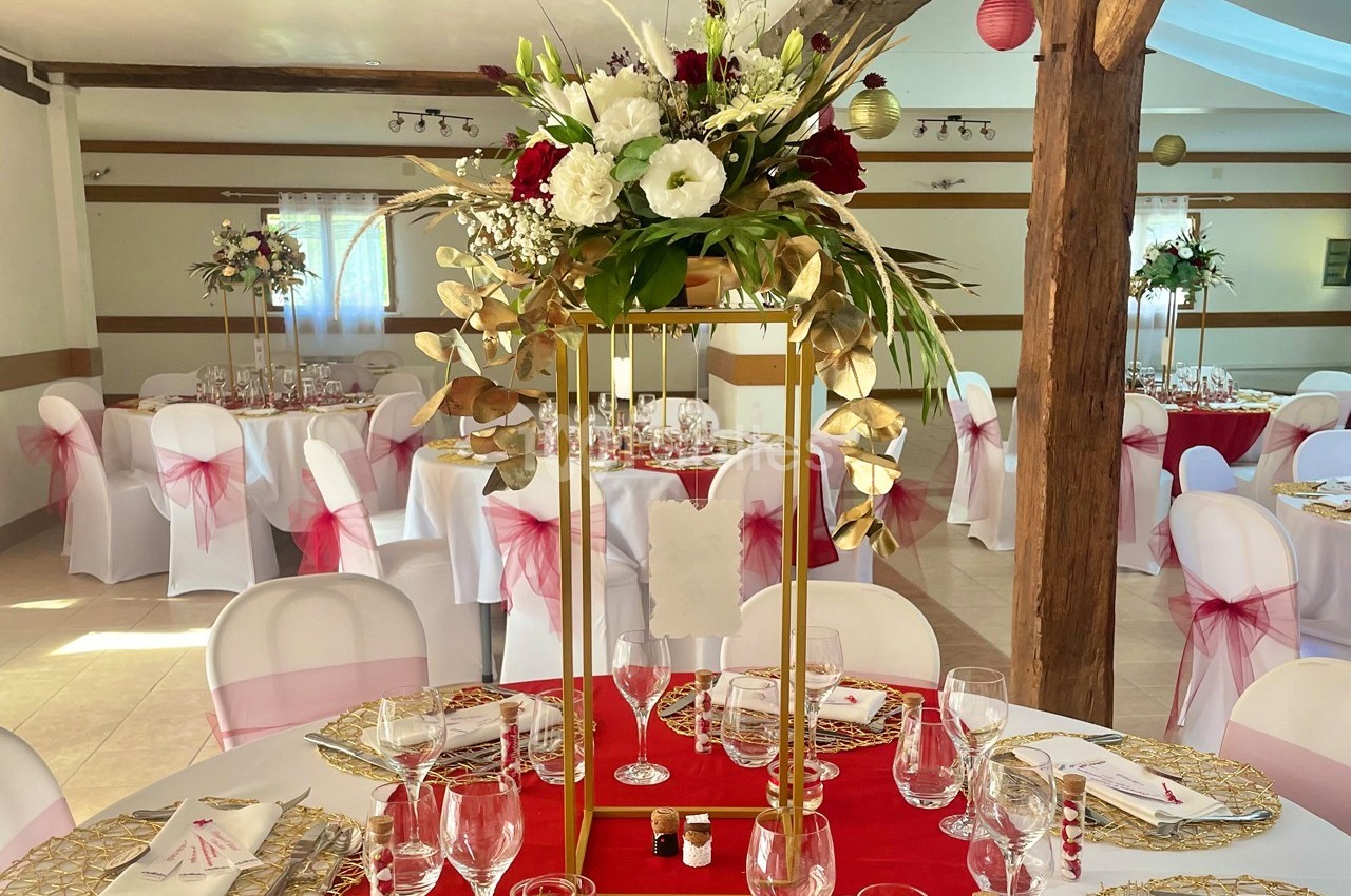 Centre de table floral avec des fleurs rouges et blanches, entouré de tables dressées pour un événement festif.
