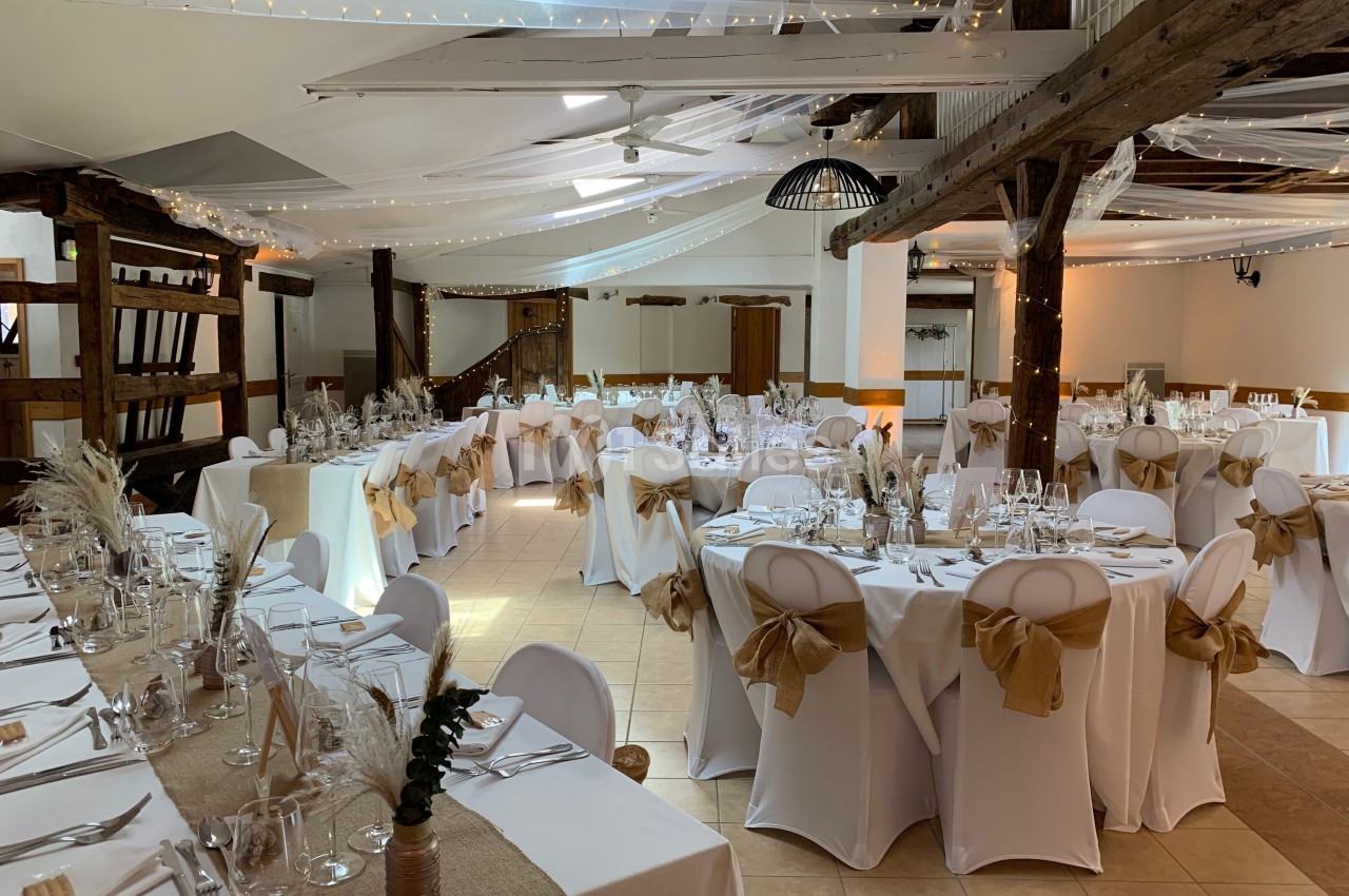 Salle de réception décorée avec des tables dressées, nappes blanches, chemins de table en jute et éclairage chaleureux.