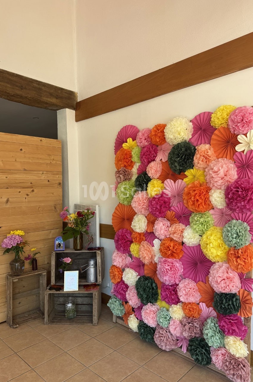 Mur décoratif avec des fleurs en papier colorées, accompagné d'une petite table en bois ornée de fleurs fraîches.