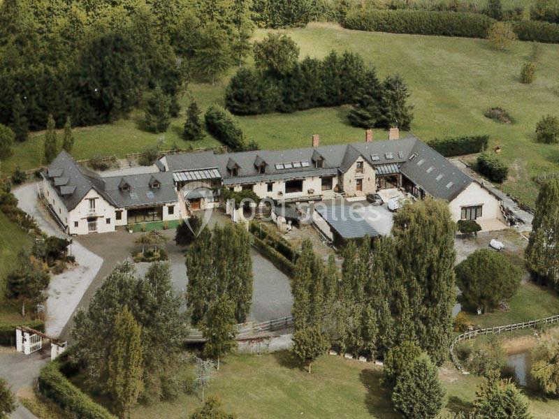 Vue aérienne d'un grand domaine rural avec plusieurs bâtiments entourés d'arbres et de prairies.