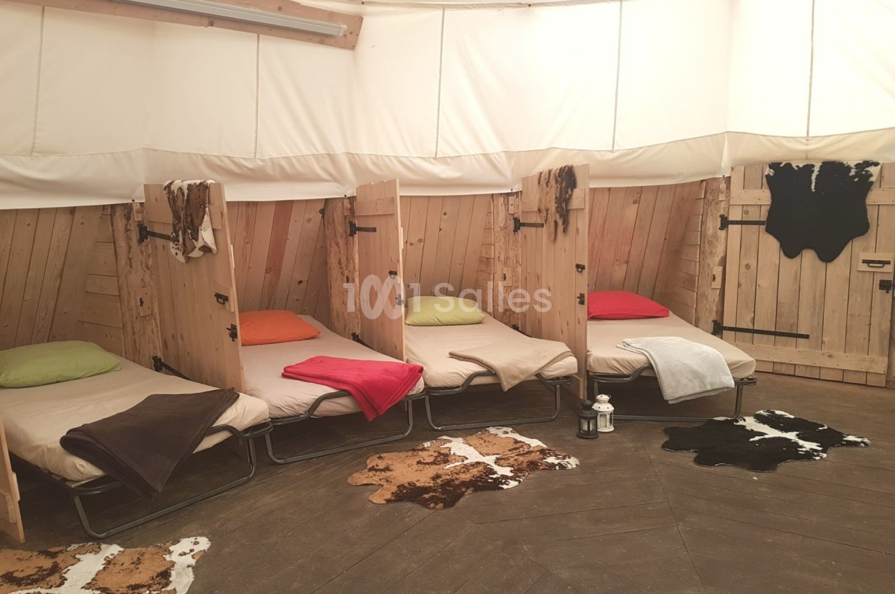 Quatre lits simples avec couvertures colorées dans une pièce circulaire en bois, décorée de tapis en peau.