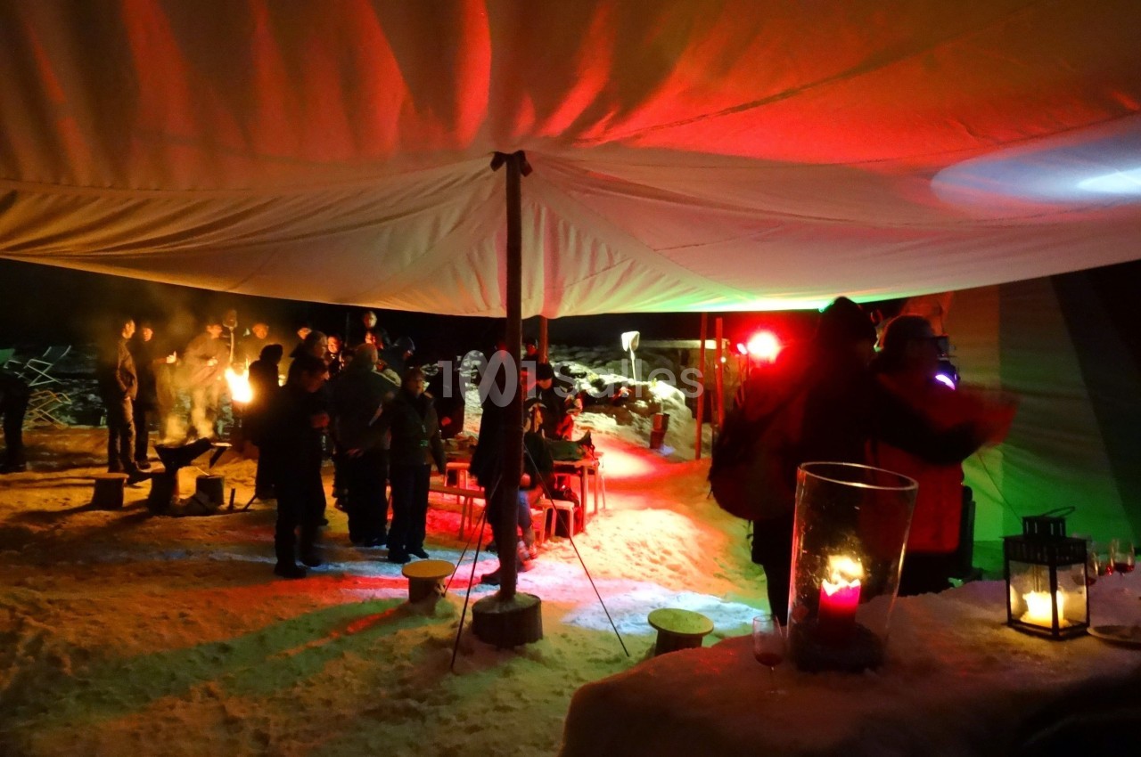 Groupe de personnes rassemblées sous une tente éclairée de lumières colorées, dans un environnement enneigé.