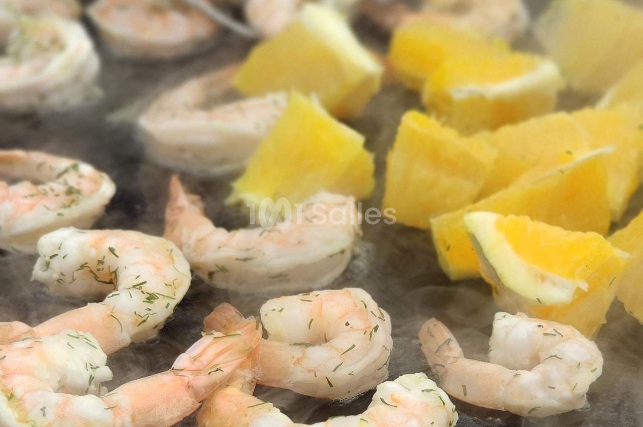 Crevettes grillées et morceaux d'ananas frais cuits sur une plaque chaude, légèrement saupoudrés d'herbes.