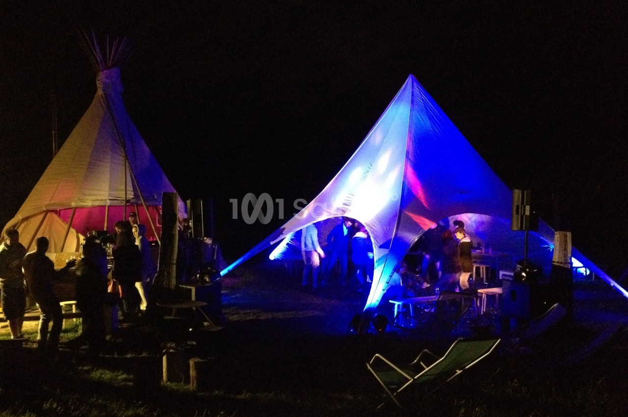 Tentes éclairées par des lumières colorées lors d'un événement nocturne en extérieur avec des participants.