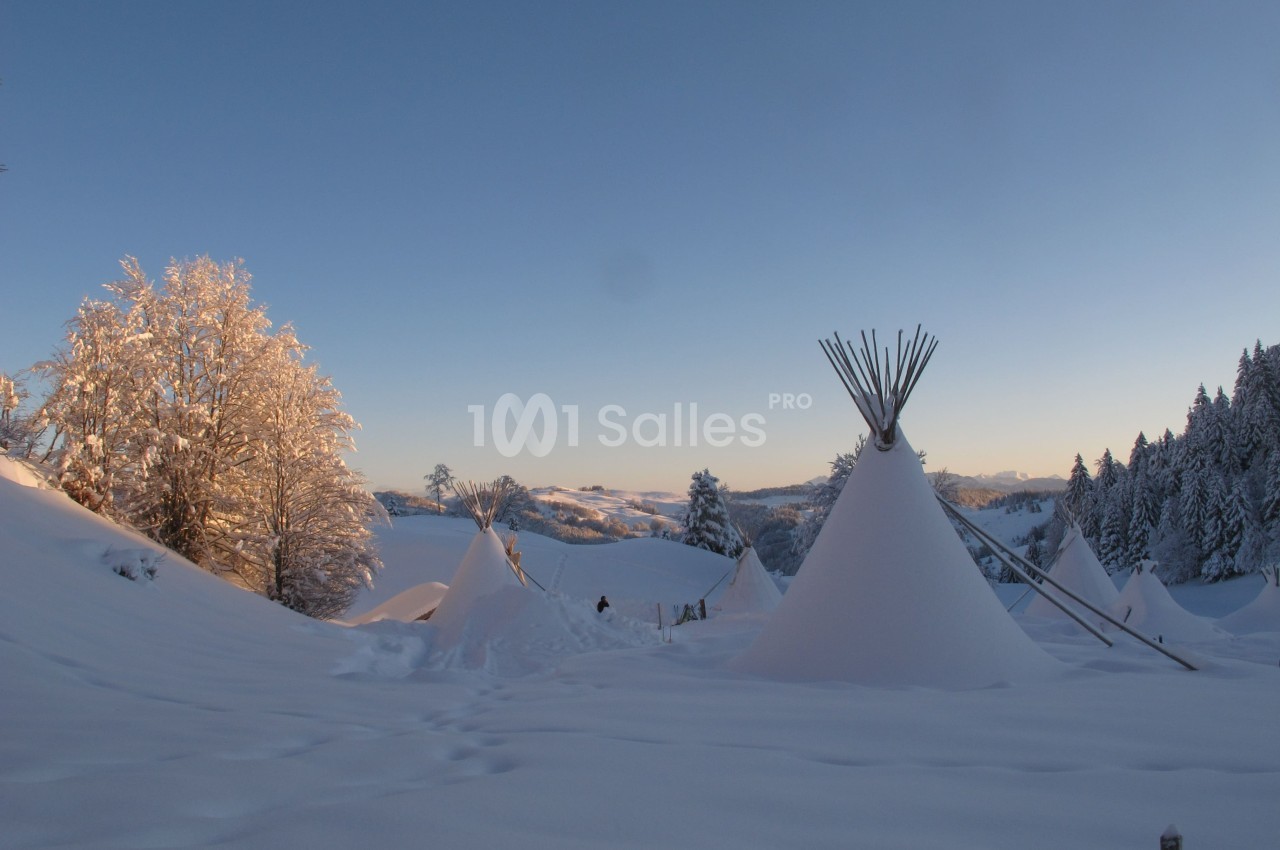 Paysage enneigé au coucher du soleil avec des tipis entourés d'arbres givrés et de collines.