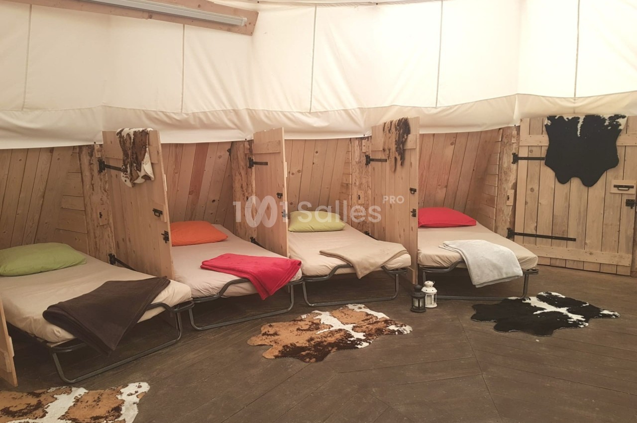 Quatre lits simples avec couvertures colorées dans une pièce circulaire en bois, décorée de tapis en peau.